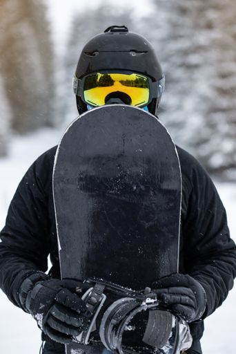 A shallow focus vertical view of a young girl snowboarder holding her snowboard in the mountains
