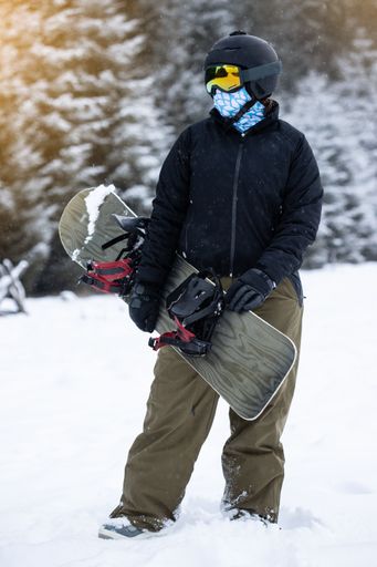 A vertical shot of a snowboarder holding her snowboard in the mountains