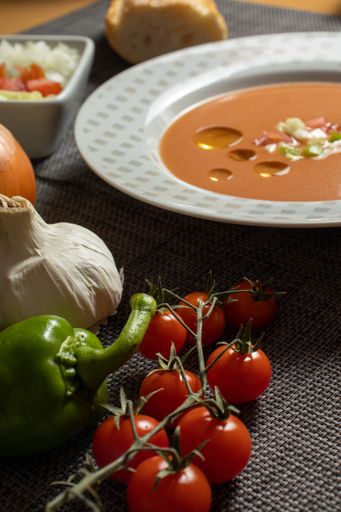 A vertical shot of gazpacho soup with its ingredients and bread