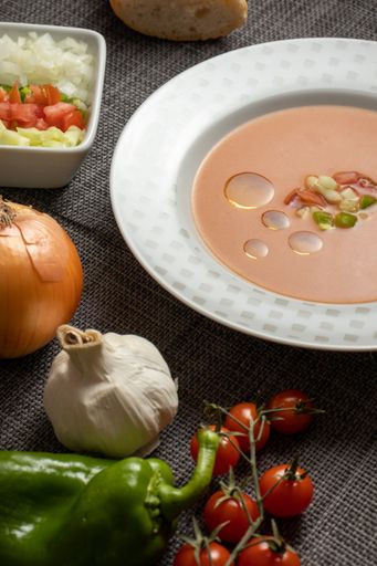 A vertical shot of gazpacho soup with its ingredients and bread