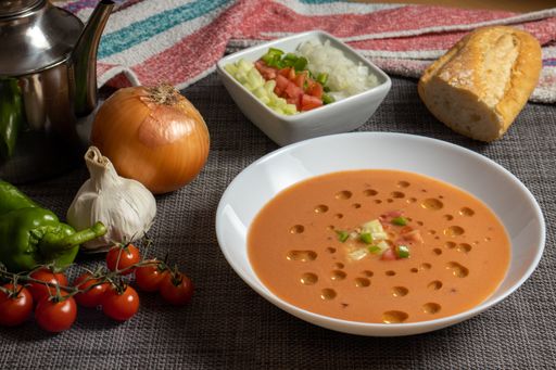 A closeup shot of gazpacho soup with its ingredients and bread