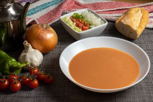 A closeup shot of gazpacho soup with its ingredients and bread