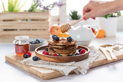 A selective focus shot of delicious pancakes with fresh blueberries, strawberries and honey on a plate