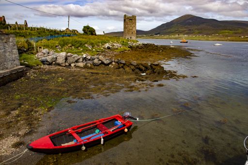 A blue and red boat on a loch surrounded by mountains and valleys under a cloudy sky In Ireland