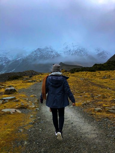 A back view of a female hiker walking through a trekking path surrounded by beautiful nature scenes