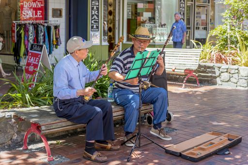 Two old street musicians sitting on a bench in the streets of Wellington and playing instruments
