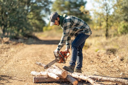 A young Caucasian man cutting a tree trunk with a chainsaw