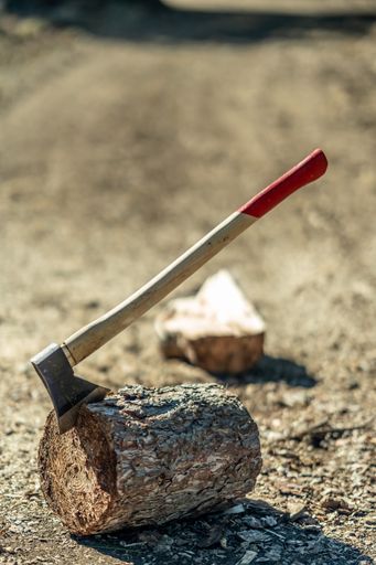 A vertical shot of an axe on a tree trunk on background of a roadway