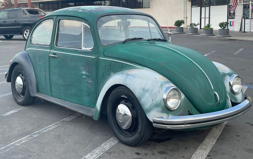An old retro green and white Volkswagen Bug in the parking lot during the daytime