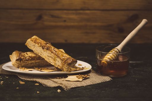 A puff pastry next to honey glass with a dipper