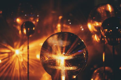 A closeup of a small disco ball under red lights surrounded by disco balls with a blurry background