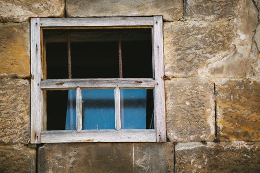 A closeup look of a wooden window with blue window reflections of an old abandoned stone building