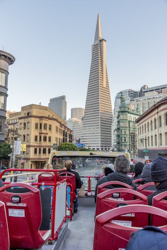 A red tourist bus riding in San Francisco under a blue sky with modern skyscrapers around it