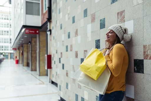 A woman in a wool hat with shopping bags smiling near a wall