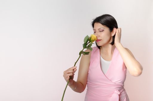 A Latino brunette with a pink shirt holding a single yellow rose and posing for the camera