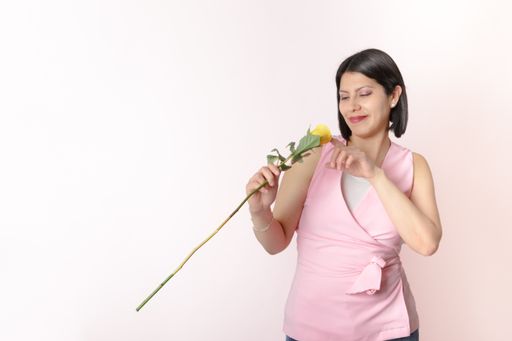 A Latino brunette with a pink shirt holding a single yellow rose and posing for the camera