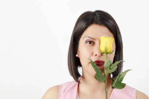 A Latino brunette with a pink shirt holding a single yellow rose and posing for the camera