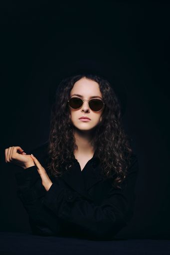 A vertical shot of a young curly female wearing sunglasses and posing on a black background