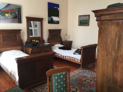 A room with two wooden beds and paintings on the walls with carpets on the floor in Hungary