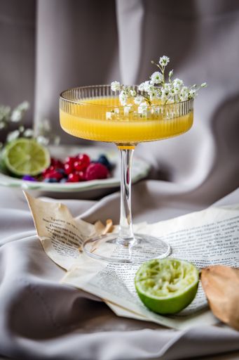 A vertical of an orange cocktail decorated with flowers with a plate full of fruits in background