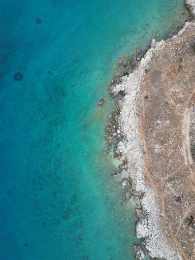 A vertical top view of bright blue seawater on a rocky shore in Croatia