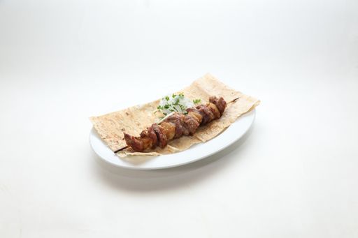 A plate with a kebab on a skewer, onions, and greens on flatbread isolated on a white background