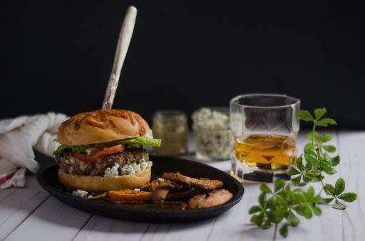 A high angle shot of a delicious juicy beef burger with a drink on a white surface