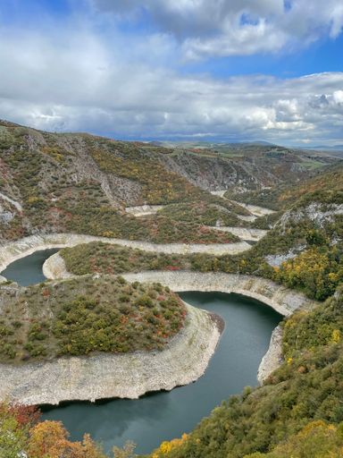 A scenic vertical view of a river flowing between evergreen cliffs against a blue cloudy sky