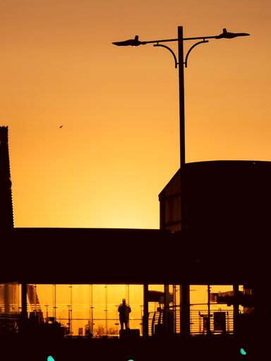 A vertical silhouette shot of a man standing in an airport window during sunset