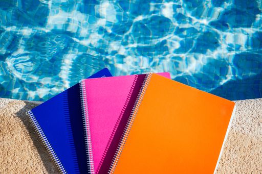 A selective focus shot of colorful notebooks near the swimming pool under the sunlight