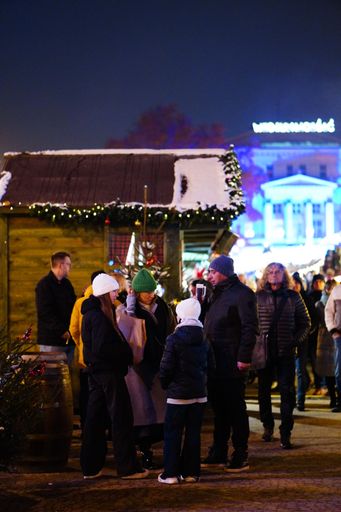The people standing by wooden huts at a Christmas market in the Plac Wolnosci square at night in Poznan.