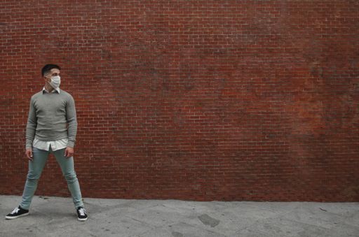 An athletic young man posing in front of a wall wearing a sanitary mask-concept of the new normal
