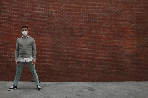 An athletic young man posing in front of a wall wearing a sanitary mask-concept of the new normal