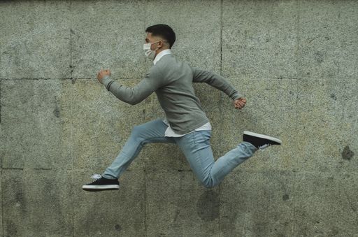 An athletic young man doing a jump wearing a sanitary mask-concept of the new normal