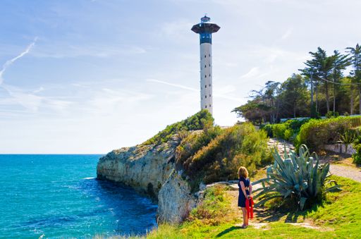 A young female in blue dress walking on the path that leads to Torredembarra lighthouse