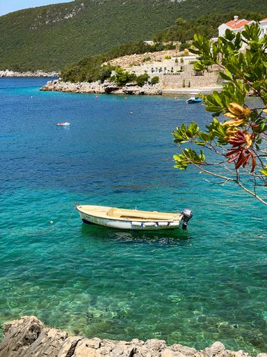 A vertical shot of a boat in the sea with green hills in the background