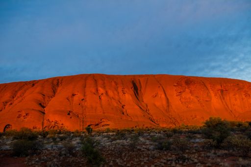 A landscape of an orange mountain with hollows surrounded by greenery under a blue sky during sunset