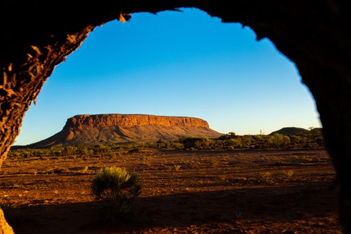 A rock arch with a view of a high mountain, land and greenery under a blue sky