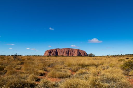 A landscape of a valley covered in dried grass with a mountain on the background under a blue sky