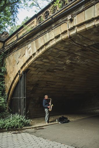 A Man playing the saxophone under an arch in dim light in Central Park in New York