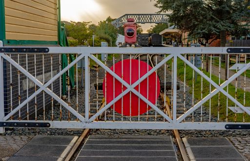 A white metal gate across the railway line next to the wooden signal house