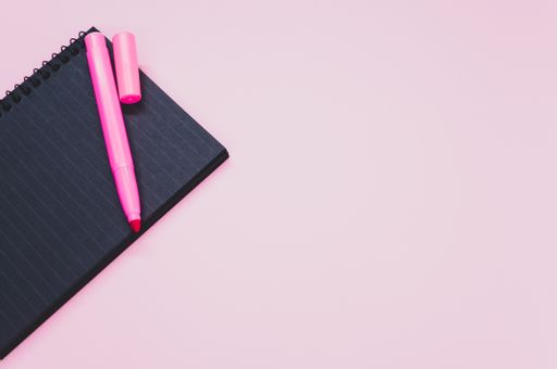 A high angle shot of a notebook and a pink marker on a pink surface