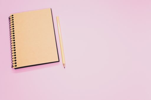 A high angle shot of a notebook and a pencil on a pink surface