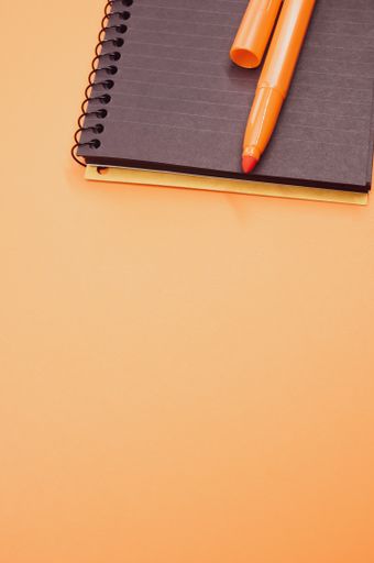 A vertical shot of a notebook and an orange marker on an orange surface