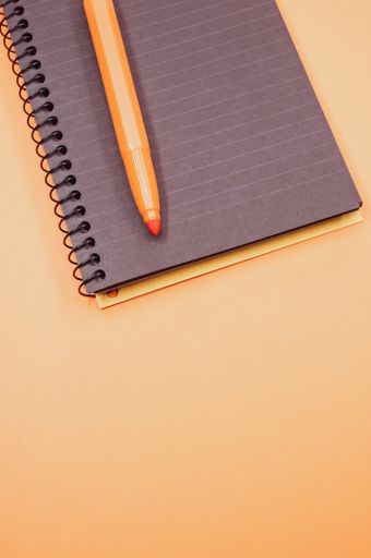A vertical shot of a notebook and an orange marker on an orange surface
