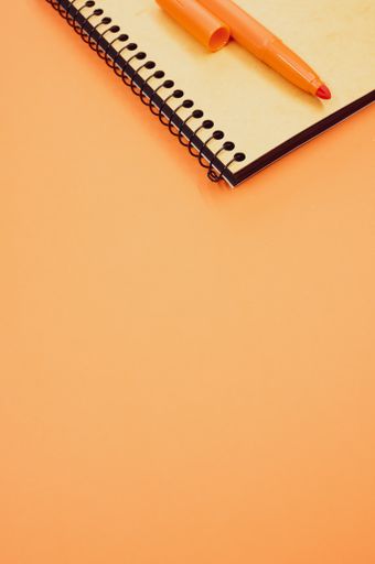 A vertical shot of a notebook and an orange marker on an orange surface
