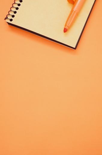 A vertical shot of a notebook and an orange marker on an orange surface