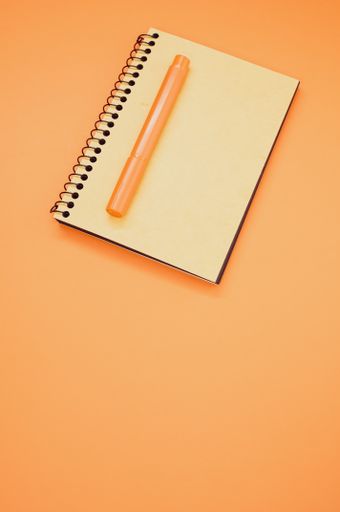 A vertical shot of a notebook and an orange marker on an orange surface