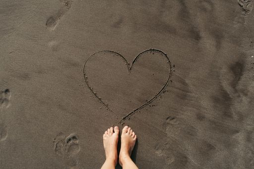 A high angle shot of a person standing on the beach near a heart on the sand