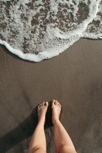A high angle shot of a person standing on the beach near seafoam